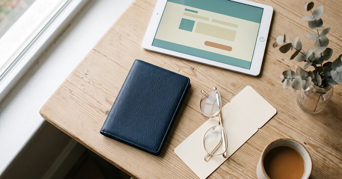 Flat lay of a passport, reading glasses, and a tablet showing a form interface on a desk
